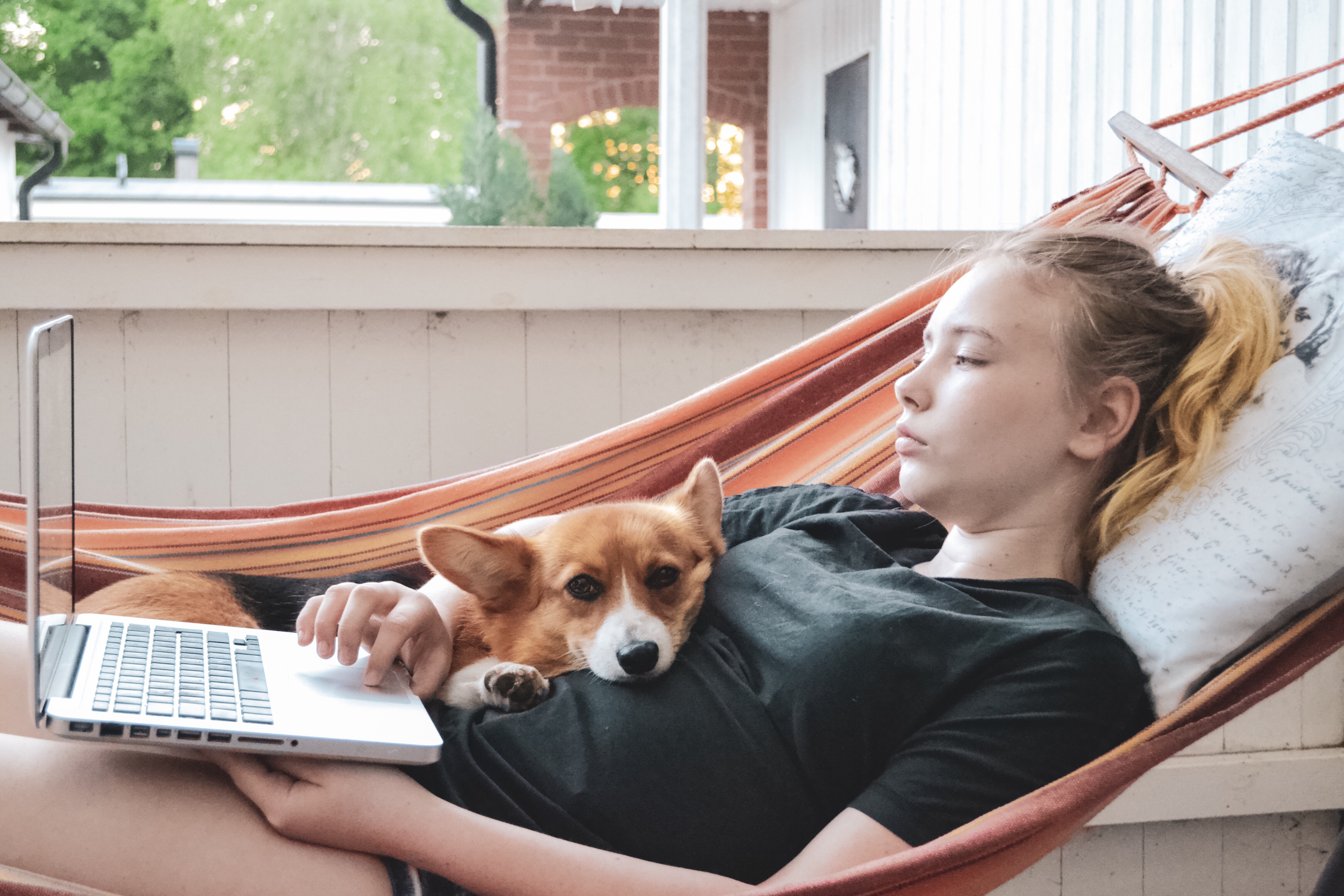 Girl sits in her hammock on her patio with her dog.