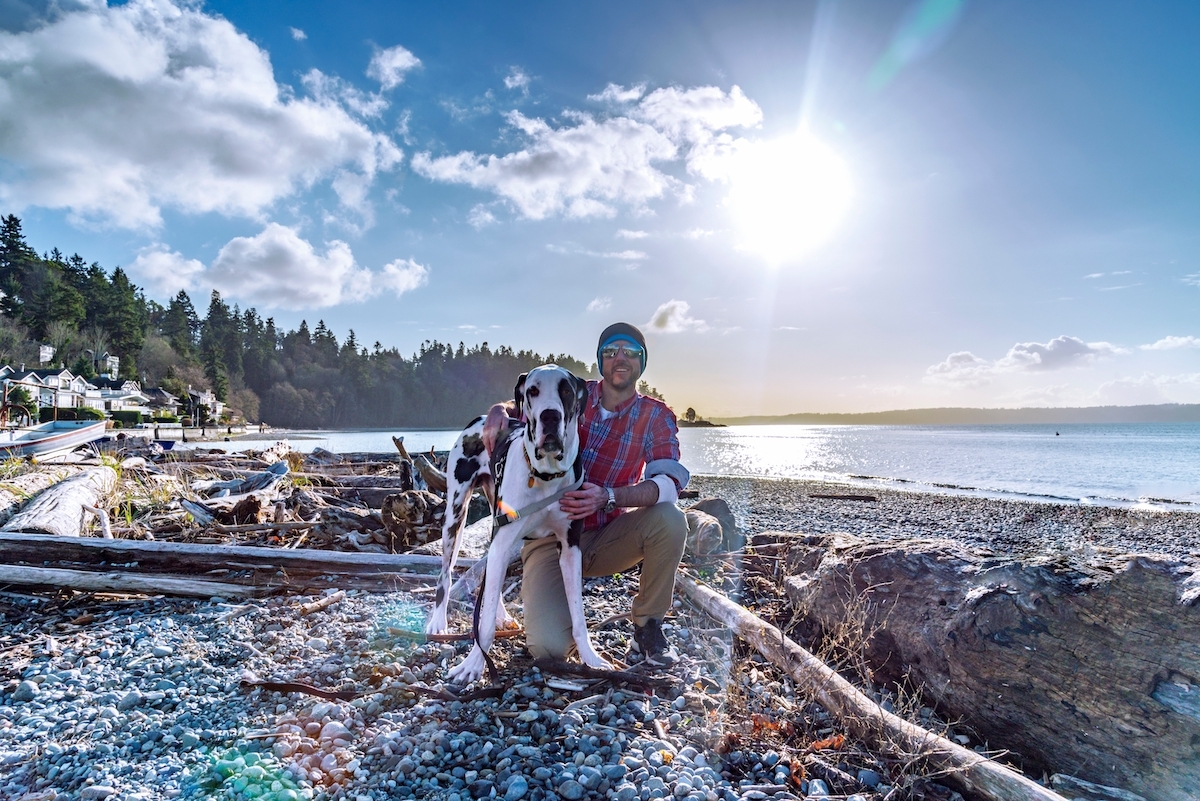 Man and his dog pose on the beach in Seattle, Washington, during the summer.